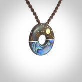 This photo shows a donut disc pendant hand carved from Lignum Vitae with premium nz paua shell, Mother of Pearl alongside; brass, copper and silver. This is a stand out one off necklace for those who appreciate art to wear. It is provided with a cord in brown that is a fixed length with Paua Shell Toggle. We ship this piece worldwide and shipping is included in the price.